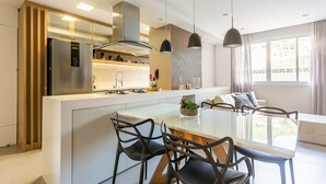 A modern kitchen with a central island, stainless steel appliances, pendant lighting, and a view to the outside. - 200m from Beiramar Shopping | WI-FI 100mb #CA43 (Florianópolis)