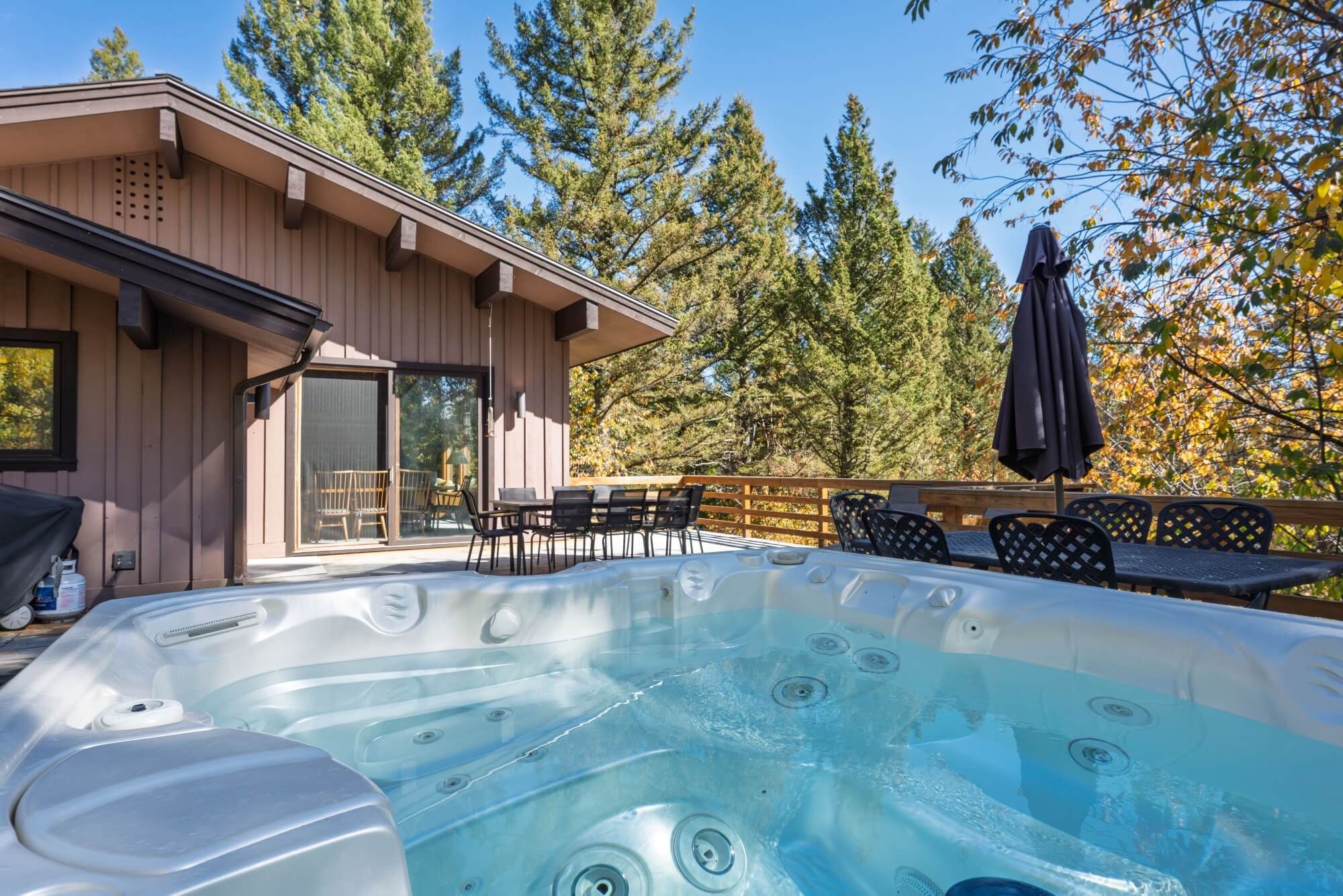 Un jacuzzi en una cabaña de madera con un área de patio, mobiliario exterior y vistas a árboles.