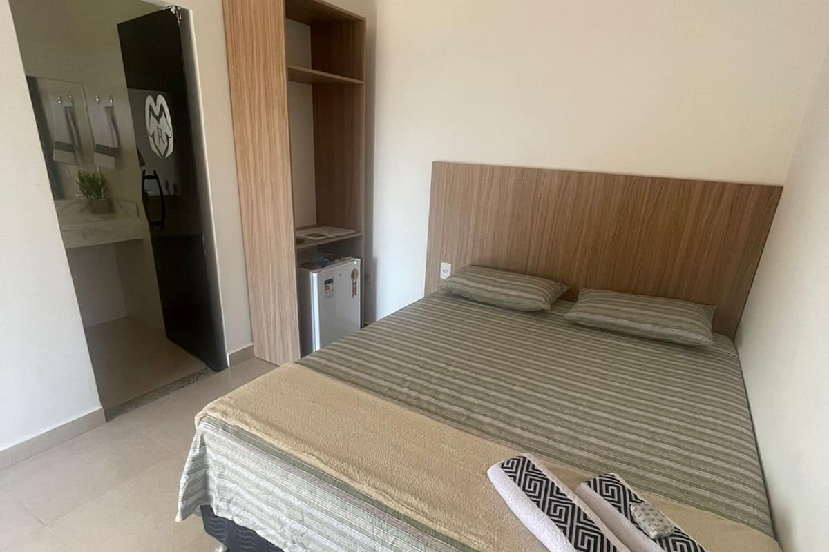 A bedroom with a bed, a wooden headboard, a bedside table, a small desk, and a wardrobe.