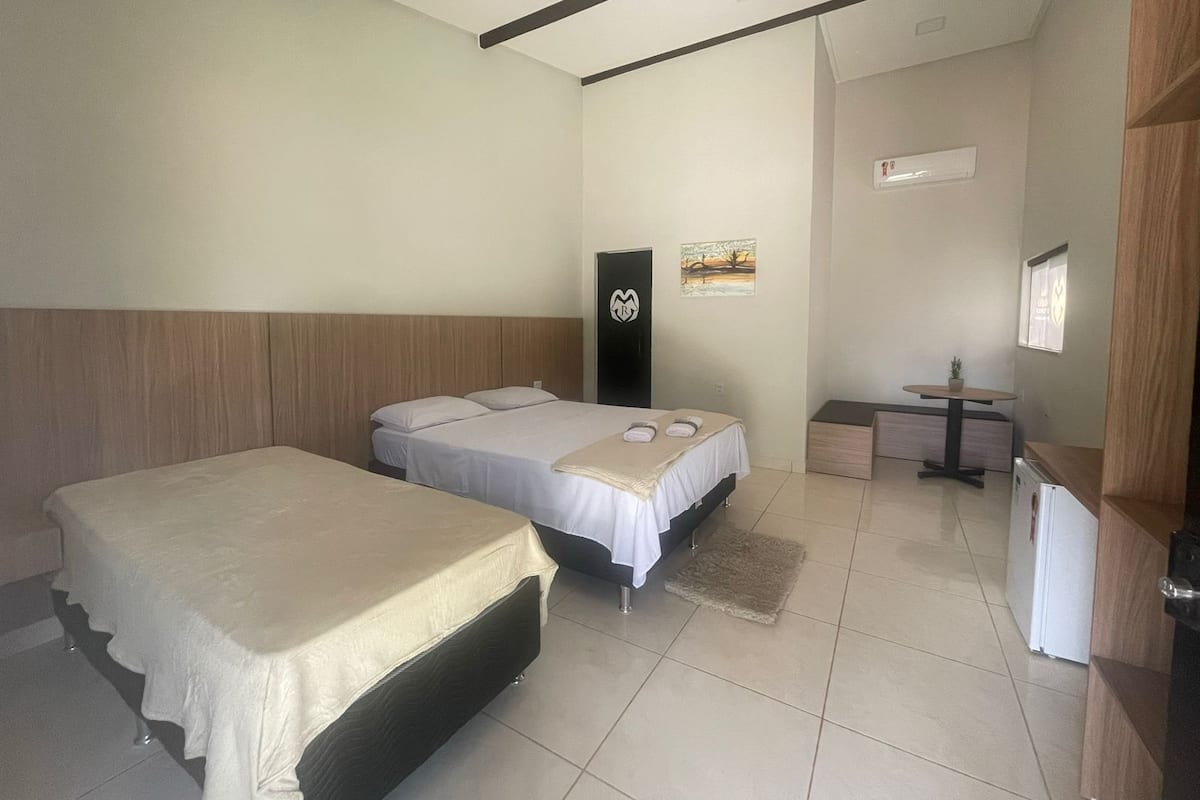 A hotel room with two beds, a small table, a refrigerator, and a painting on the wall.