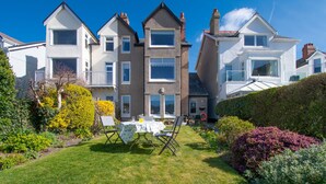 A residential property with a well-maintained lawn, a dining table with chairs, and a variety of flowering plants. - Sandbanks - Two Bedroom Cottage, Sleeps 3 (Deganwy)