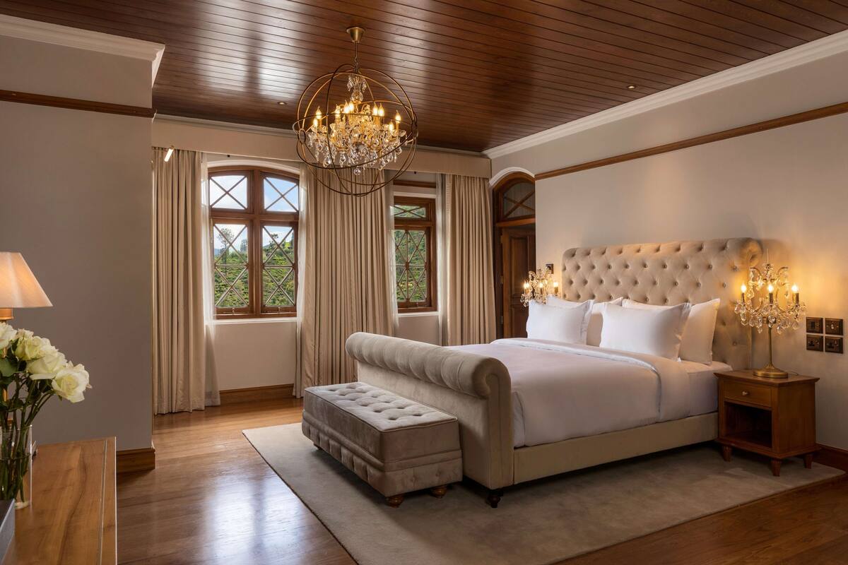 Ein Schlafzimmer mit einem großen Bett, einem gepolsterten Kopfteil, Holzboden und einem Chandelier.