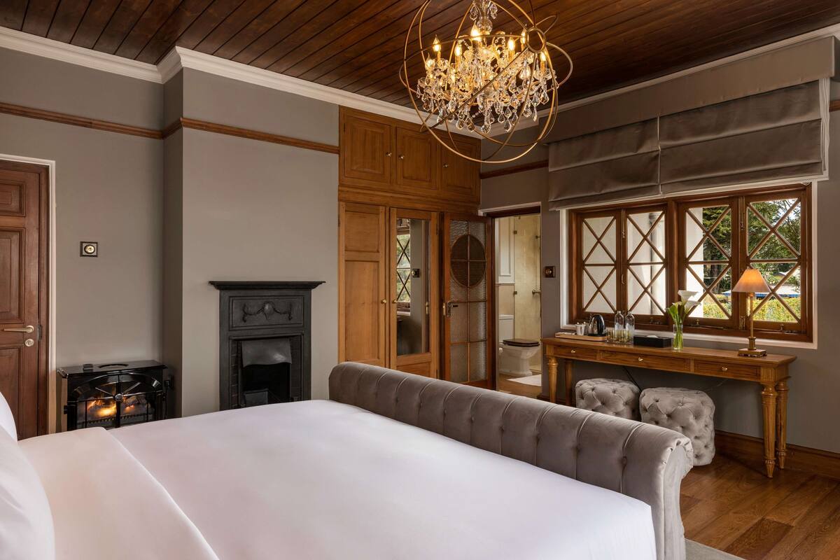 Ein Schlafzimmer mit einem großen Bett, einem Kamin, einem Holztisch und einem Fenster mit Blick.