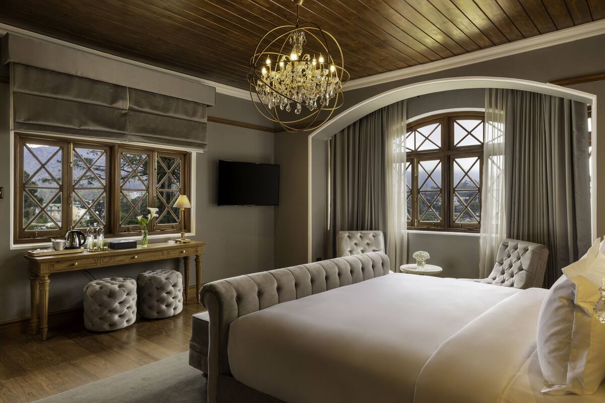 Ein Schlafzimmer mit einem großen Bett, einer Kristallleuchtre, einem Fernseher und Bergblick.