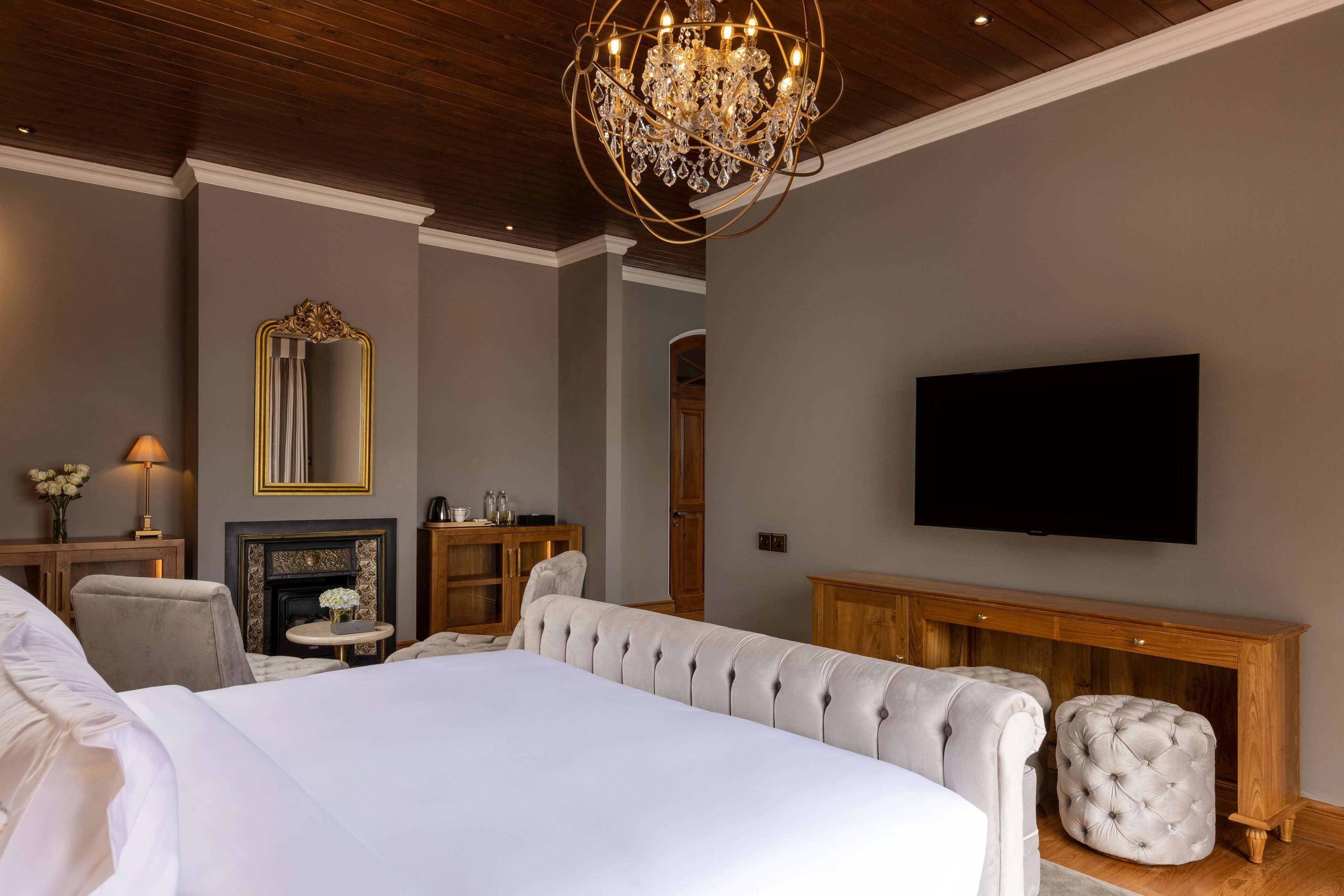 A bedroom with a large bed, a chandelier, a television, and a fireplace.