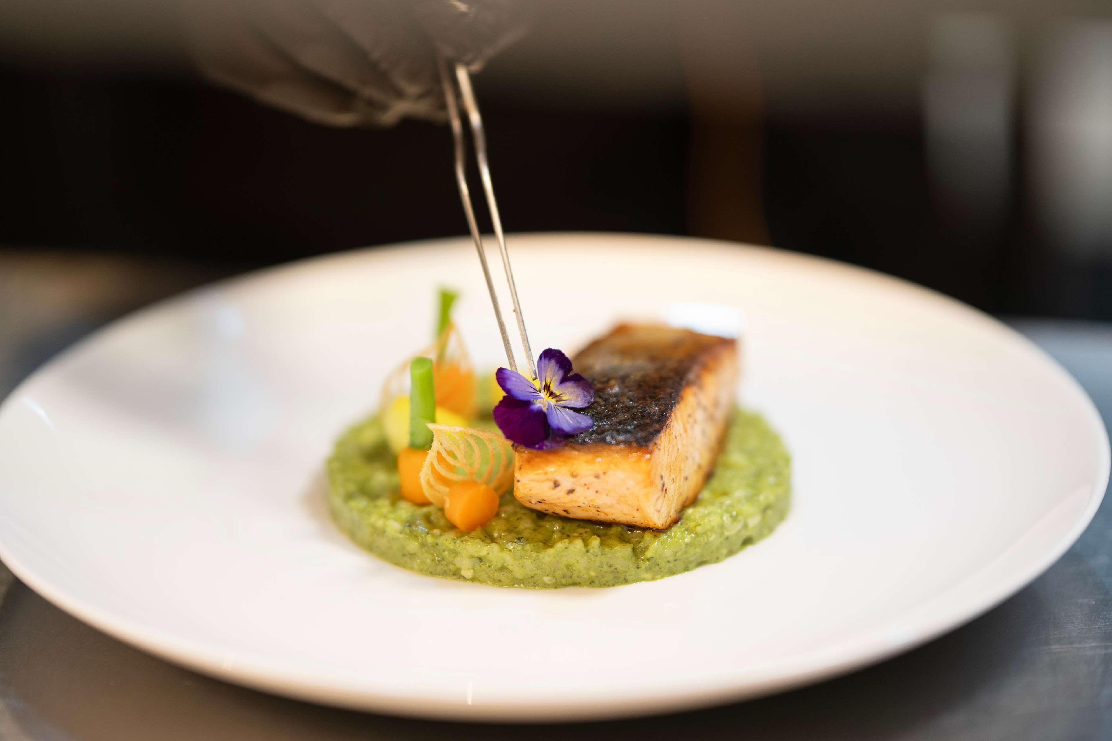 A plate with a piece of salmon, green sauce, and decorative elements.