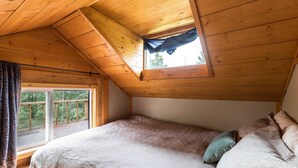 Ein Schlafzimmer mit schrägverdeckter Decke, einem großen Fenster mit Blick auf Grünflächen und einem Bett mit vielen Kissen.