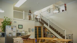 Una cocina amplia con techo alto, una escalera que conecta dos pisos y un comedor con una mesa de madera.