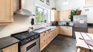 Una cocina moderna con armarios de madera, electrodomésticos de acero inoxidable, un ventanal grande y una planta en maceta.