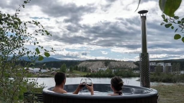 Zwei Personen in einer Badewanne mit Blick auf einen See und Berge.