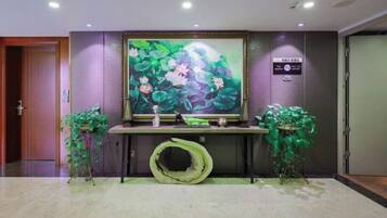 A reception area with a large floral painting, a reception desk, and two potted plants.