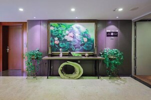 A reception area with a large floral painting, a reception desk, and two potted plants.