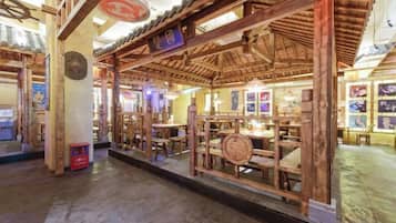 A traditional wooden structure with a thatched roof, possibly a restaurant or tea house, with tables and chairs inside.
