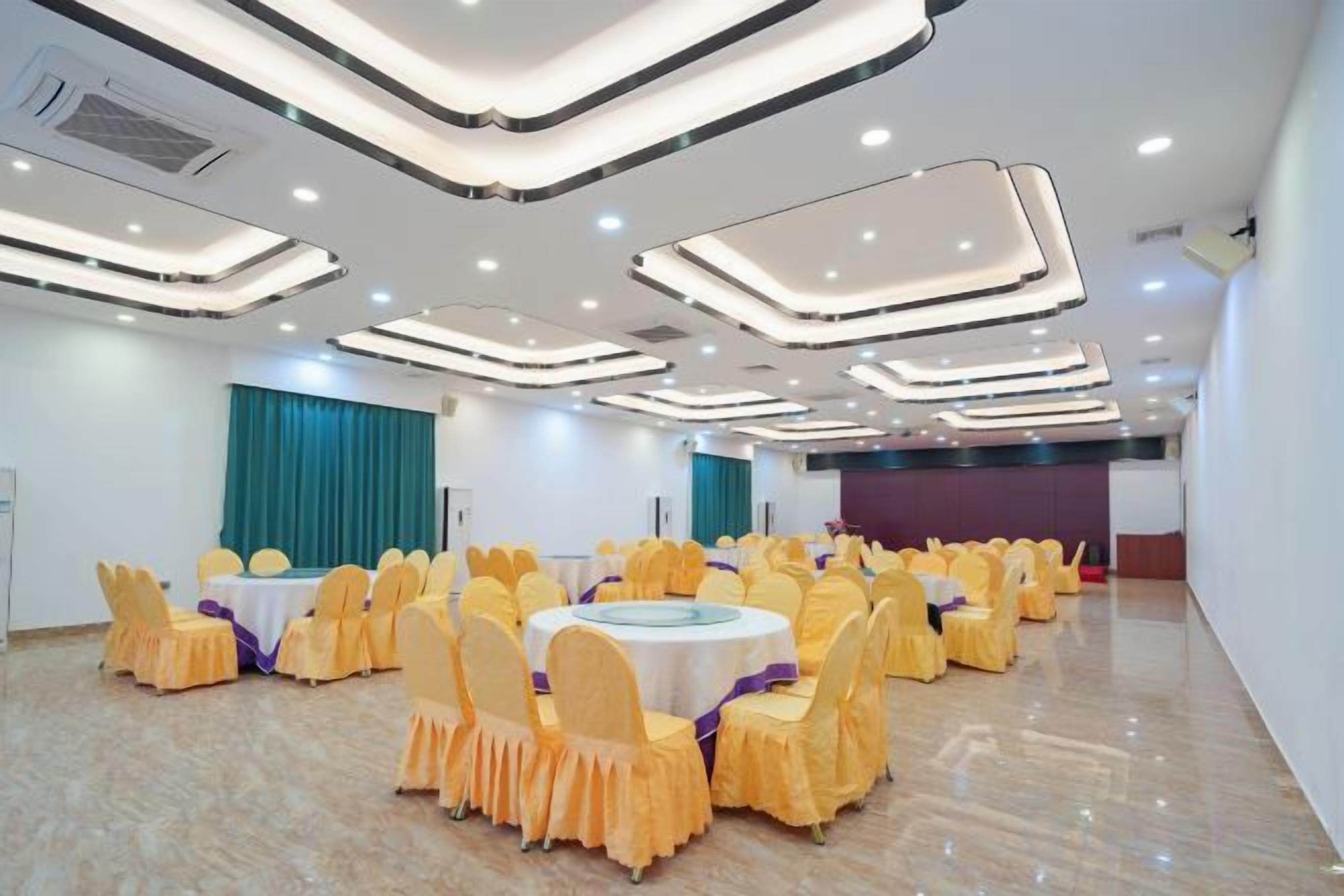 A banquet hall with round tables and yellow chairs, recessed ceiling lighting, and a marble floor.