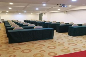 A conference room with rows of tables and chairs, carpeted floor, and a projector screen. - Huaying Wanrun Hotel (Cenxi)