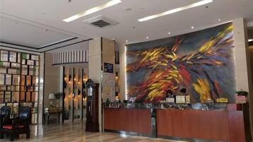 A hotel reception area with a modern design, a reception desk, and a large abstract painting on the wall.