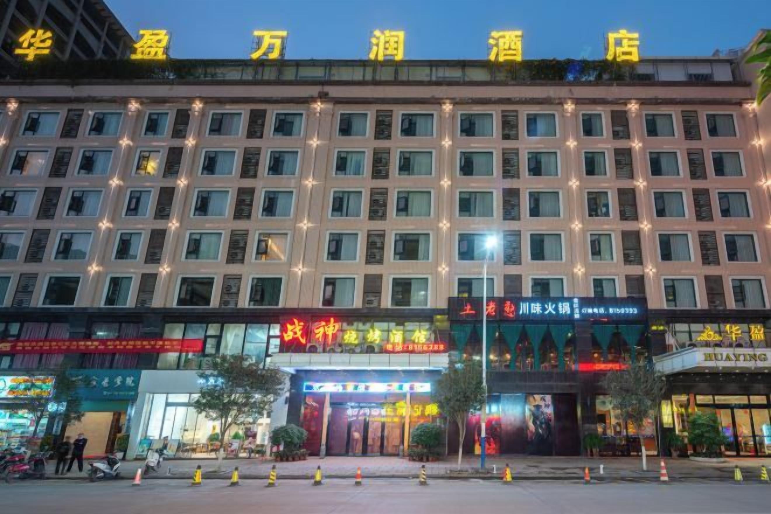 A multi-story hotel with a row of windows on each floor, a prominent entrance with signage, and a parking area in front.