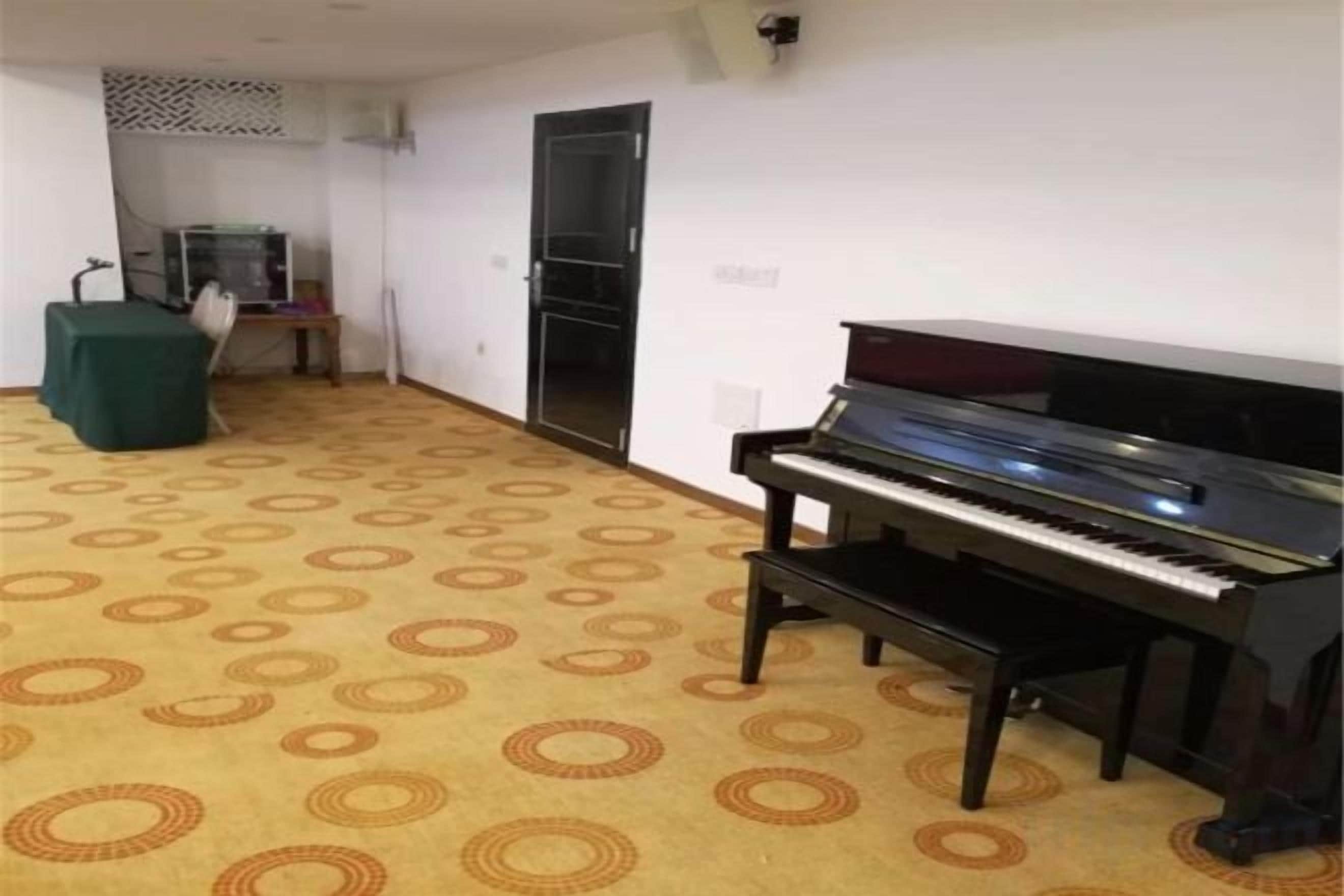 Una habitación con un piano, una alfombra estampada, una mesa verde y una puerta.