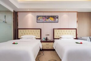 A hotel room with two beds, a bedside table with a lamp, a painting on the wall, and a carpeted floor. - Huaying Wanrun Hotel (Cenxi)