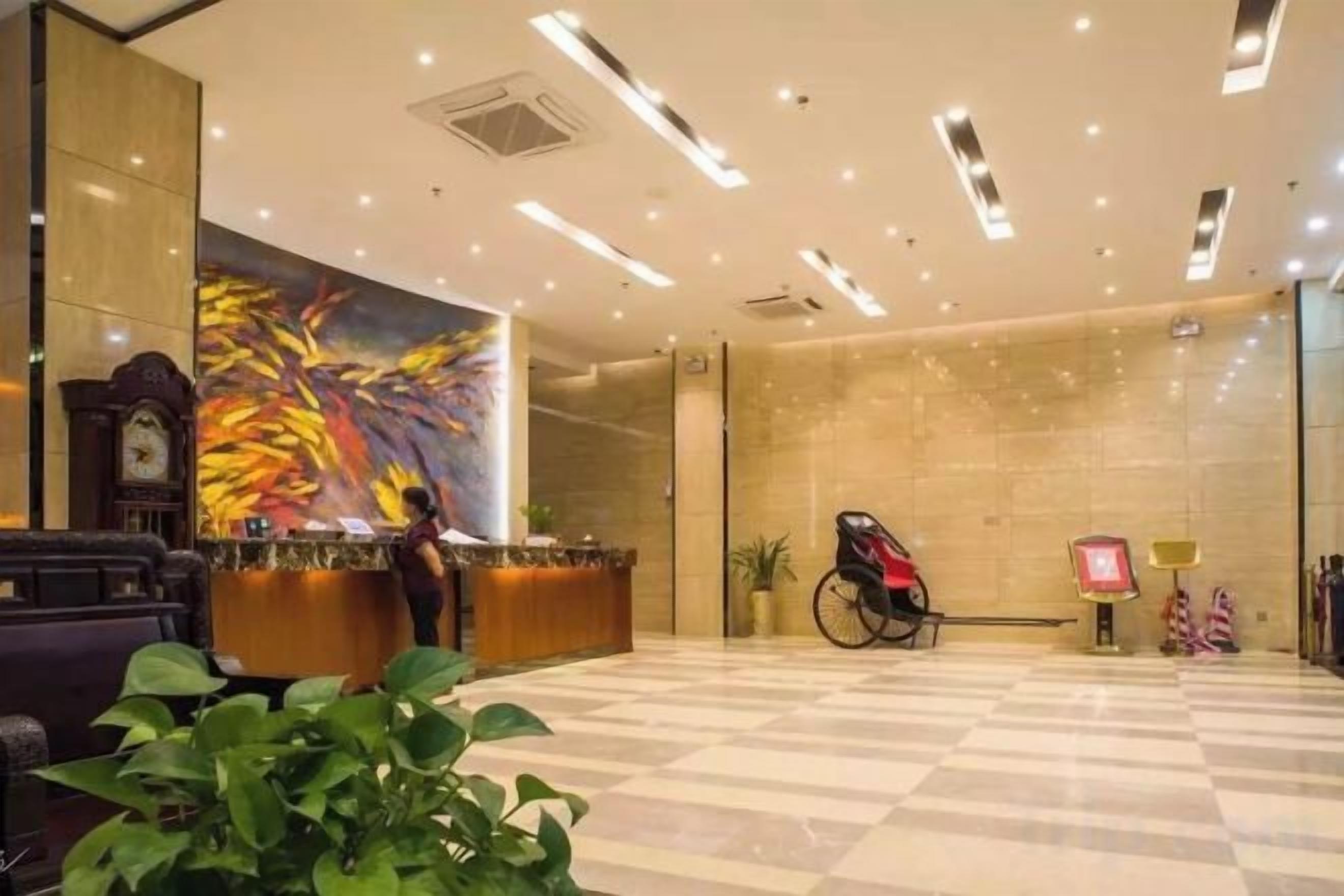A hotel lobby with a reception desk, a clock, a wheelchair, and a large abstract painting on the wall.