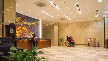 A hotel lobby with a reception desk, a clock, a wheelchair, and a large abstract painting on the wall.