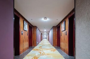 Un pasillo de hotel con puertas de madera, alfombra estampada y cuadros en las paredes.