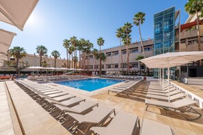 Ein Poolbereich mit Liegestühlen, Sonnenschirmen und Palmen.