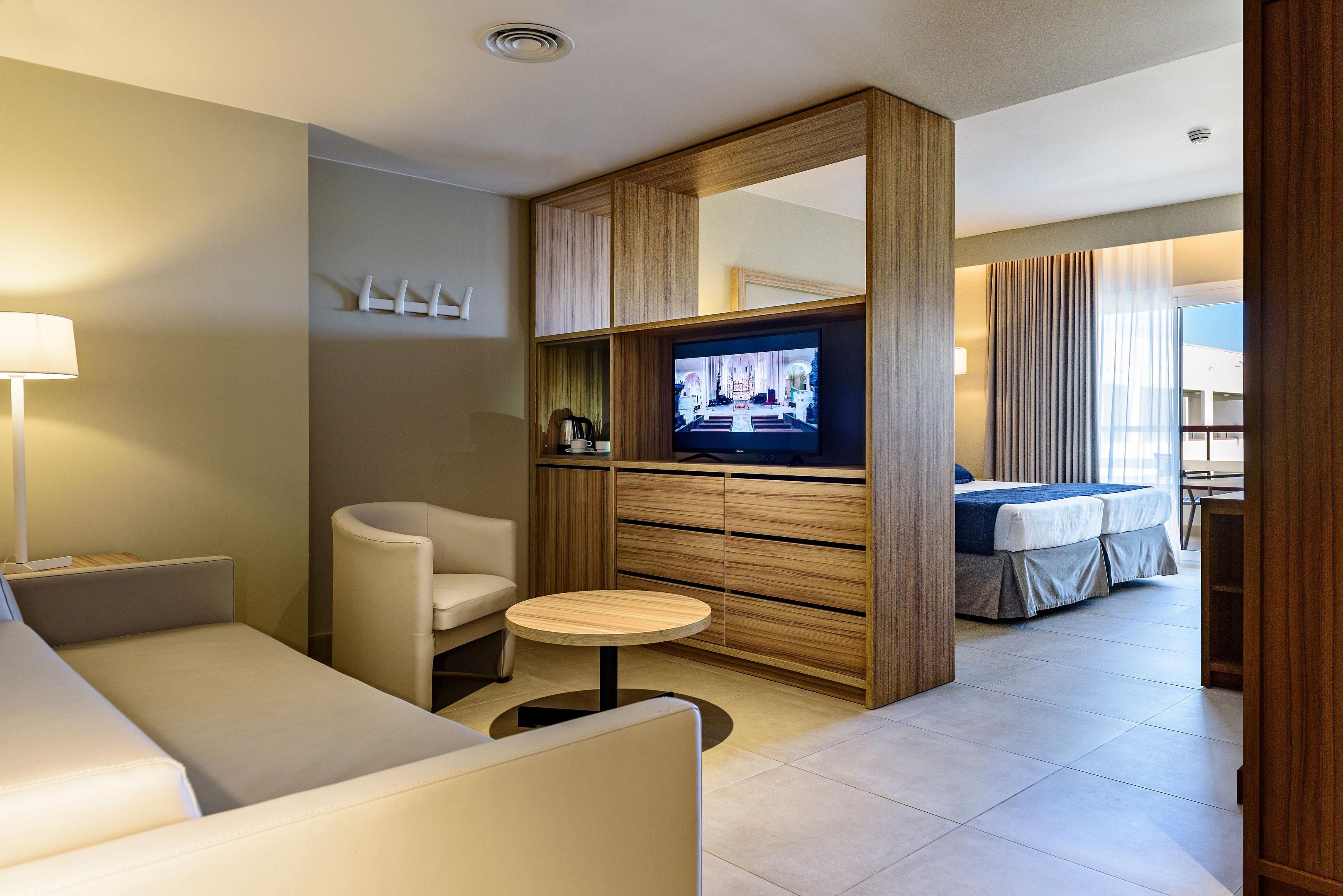Una habitación de hotel moderna con sofá, una mesita redonda, televisor, cama y un separador de madera.