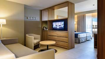 Una habitación de hotel moderna con sofá, una mesita redonda, televisor, cama y un separador de madera.