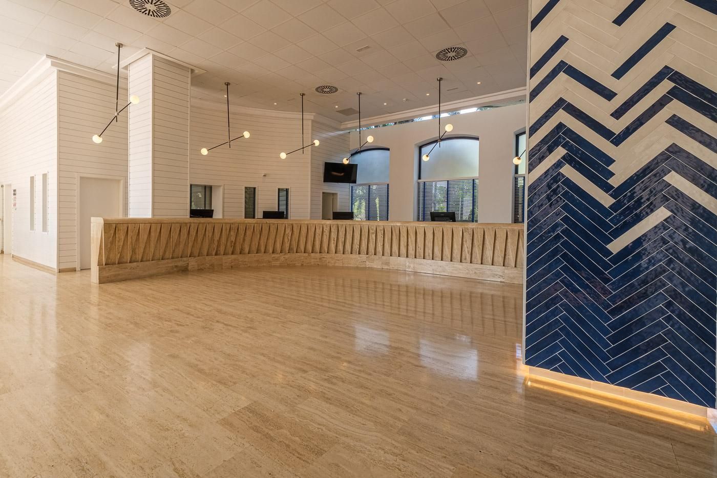 Un vestíbulo amplio con mostrador de recepción de madera, iluminación colgante moderna y un revestimiento de pared con motivo de espiga.