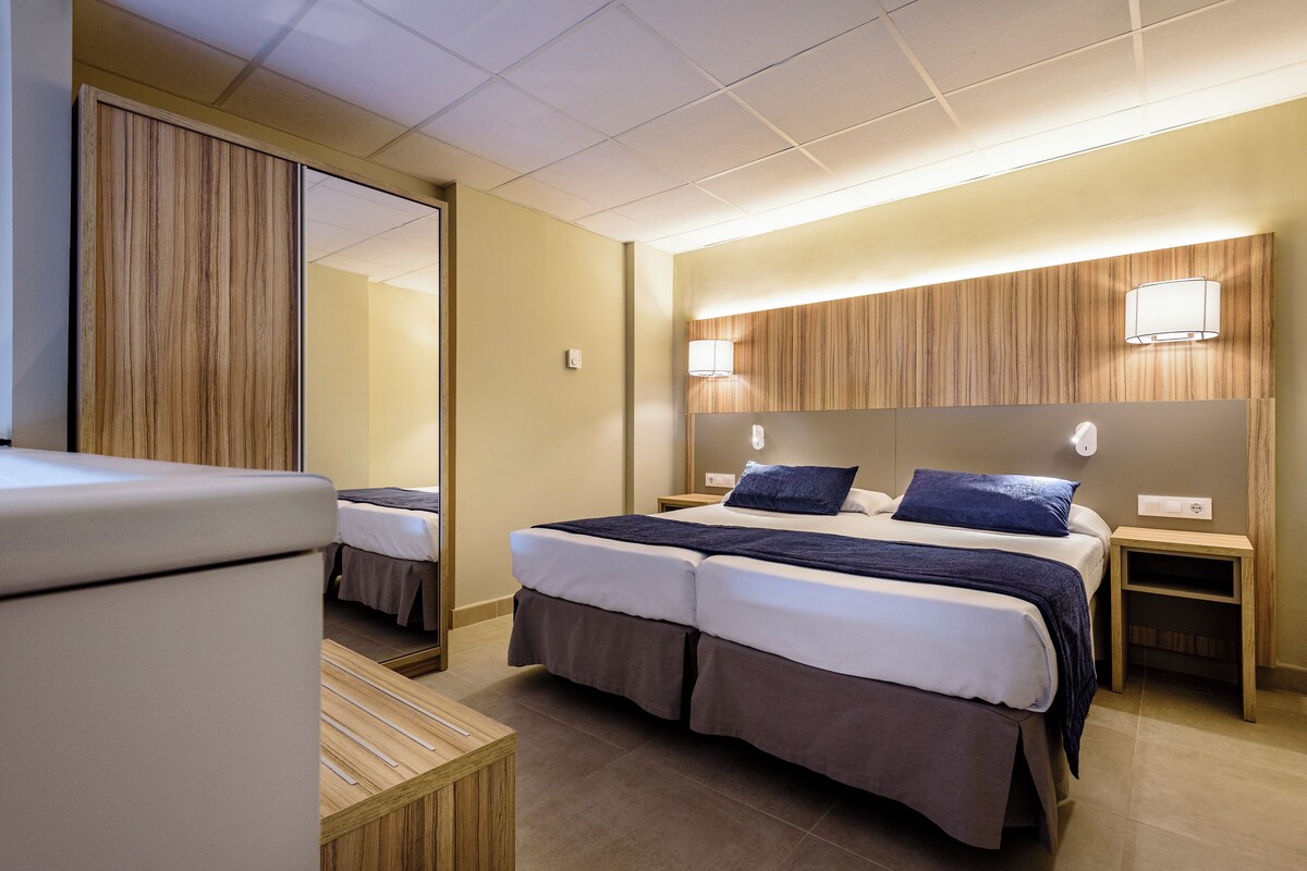 Una habitación de hotel con cama doble, dos mesitas de noche, un espejo y un armario.