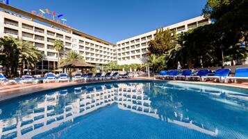 A hotel with a swimming pool, lounge chairs, and palm trees.