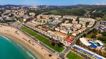 Vista aérea de un complejo turístico frente al mar, con varios edificios de hotel y una plaza central.