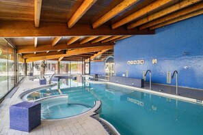 Una piscina interior con vigas de madera, paredes con azulejos y señalización clara.