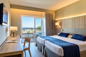 A hotel room with a bed, a desk, a chair, a TV, and a balcony with a view.