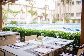 Mesa de comedor lista con un menú, copas de vino y un pequeño jarrón con flores, con vistas a una zona de piscina con sillones de descanso.