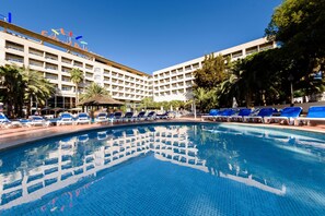 Un hotel con piscina, sillas de descanso y palmeras.