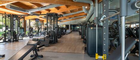 A gym with various exercise equipment, wooden ceiling beams, and a clear view of the outdoors.