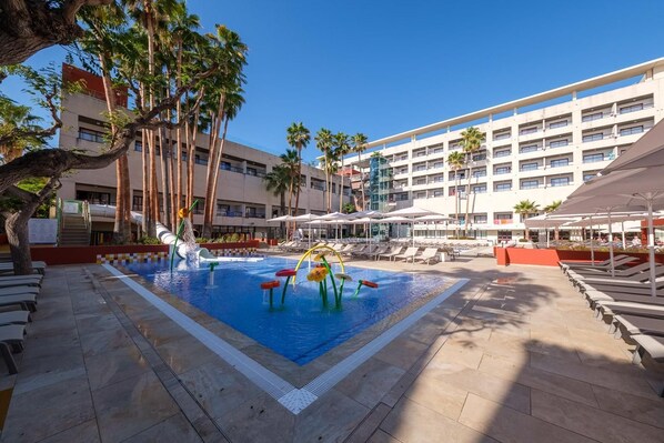 Zona de piscina de hotel con tobogán de agua, tumbonas y palmeras.