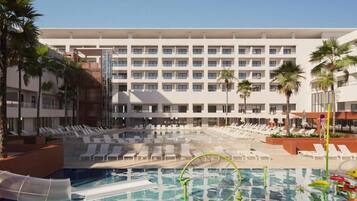 A hotel pool area with multiple lounge chairs and a large building in the background.