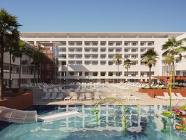 A hotel pool area with multiple lounge chairs and a large building in the background.
