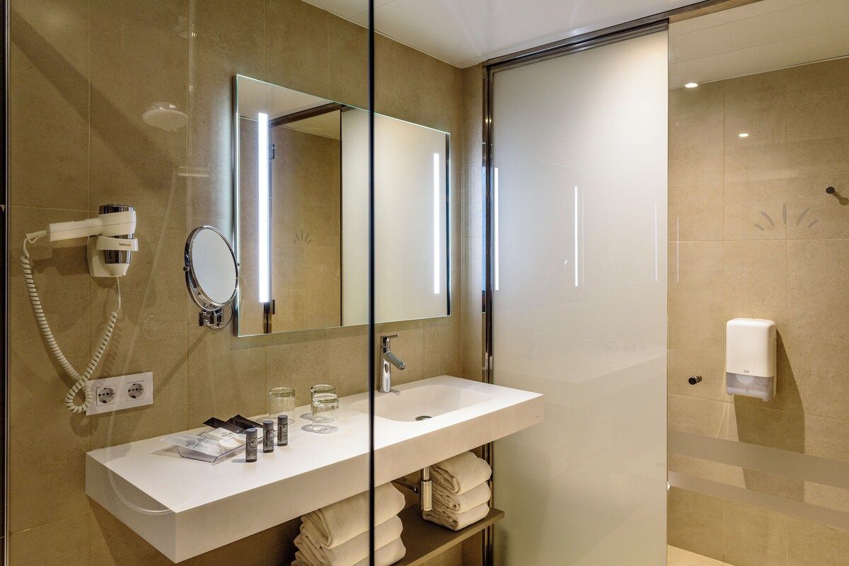 Un baño moderno con lavabo blanco, espejo, secador de pelo y cabina de ducha de vidrio.