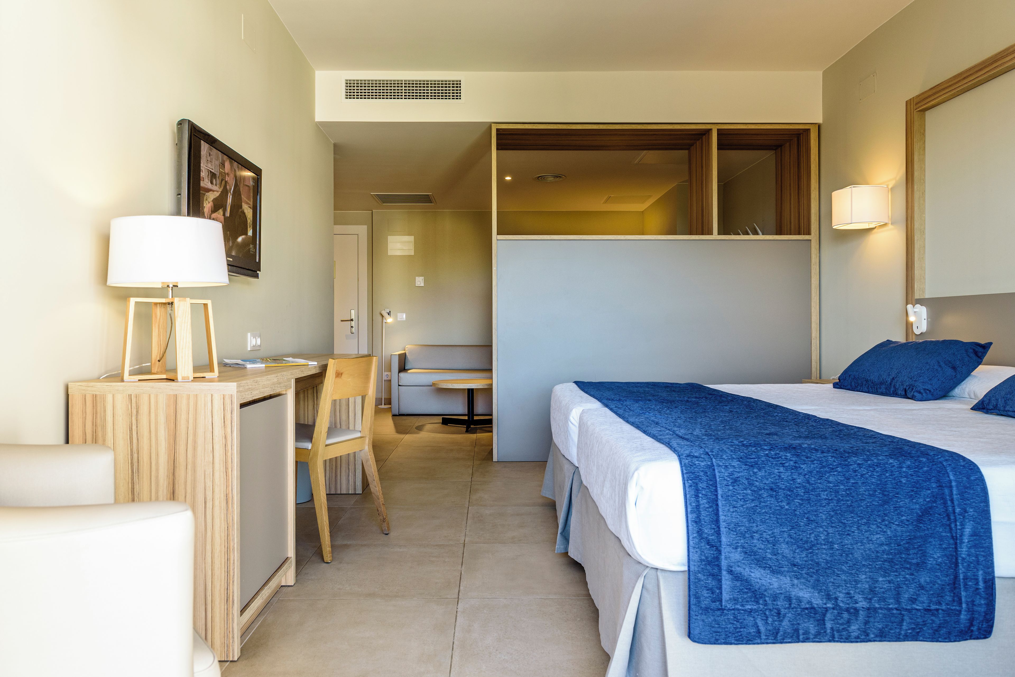 A hotel room with a bed, a desk, a chair, and a small table.