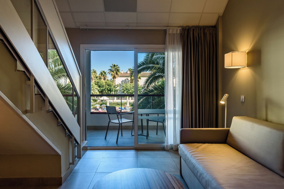 Una habitación de hotel moderna con balcón, sofá y zona de comedor con sillas.