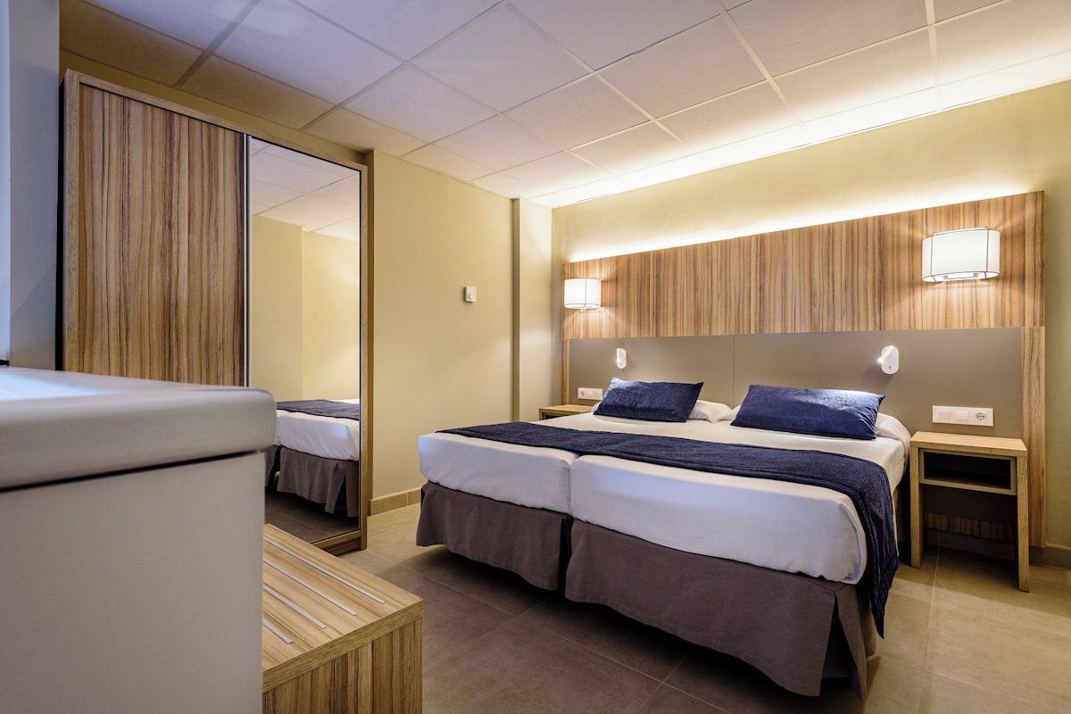 Una habitación de hotel con cama doble, dos mesitas de noche, un espejo y un armario.