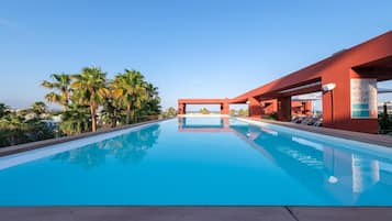 Una piscina azul cristalina con una estructura roja moderna, palmeras y un cielo despejado.