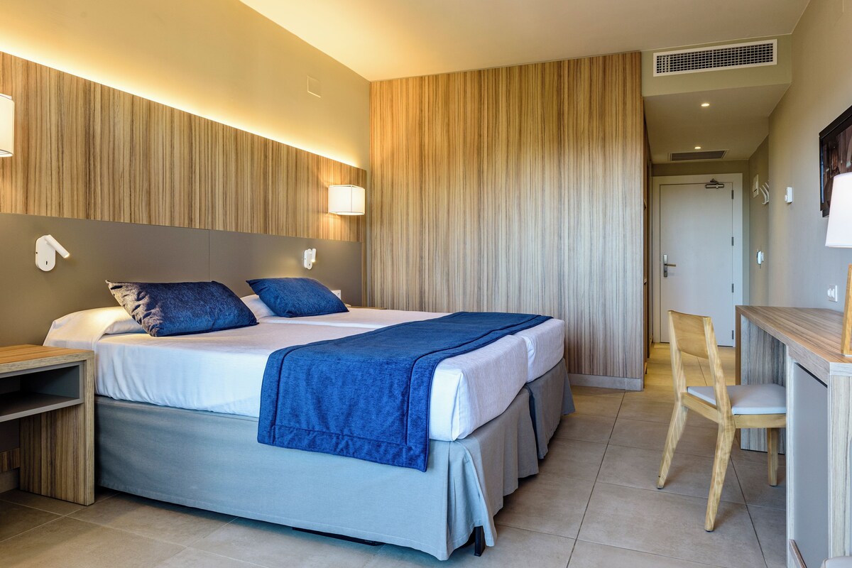 Una habitación de hotel moderna con una cama grande, mesitas de noche, un escritorio y una silla.
