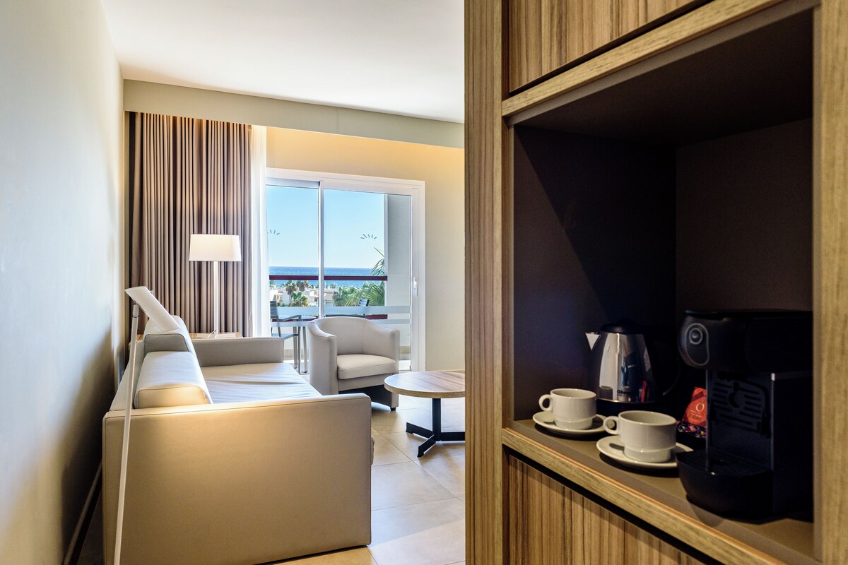 Habitación de hotel con sofá, una mesita, cafetera y vistas al exterior.