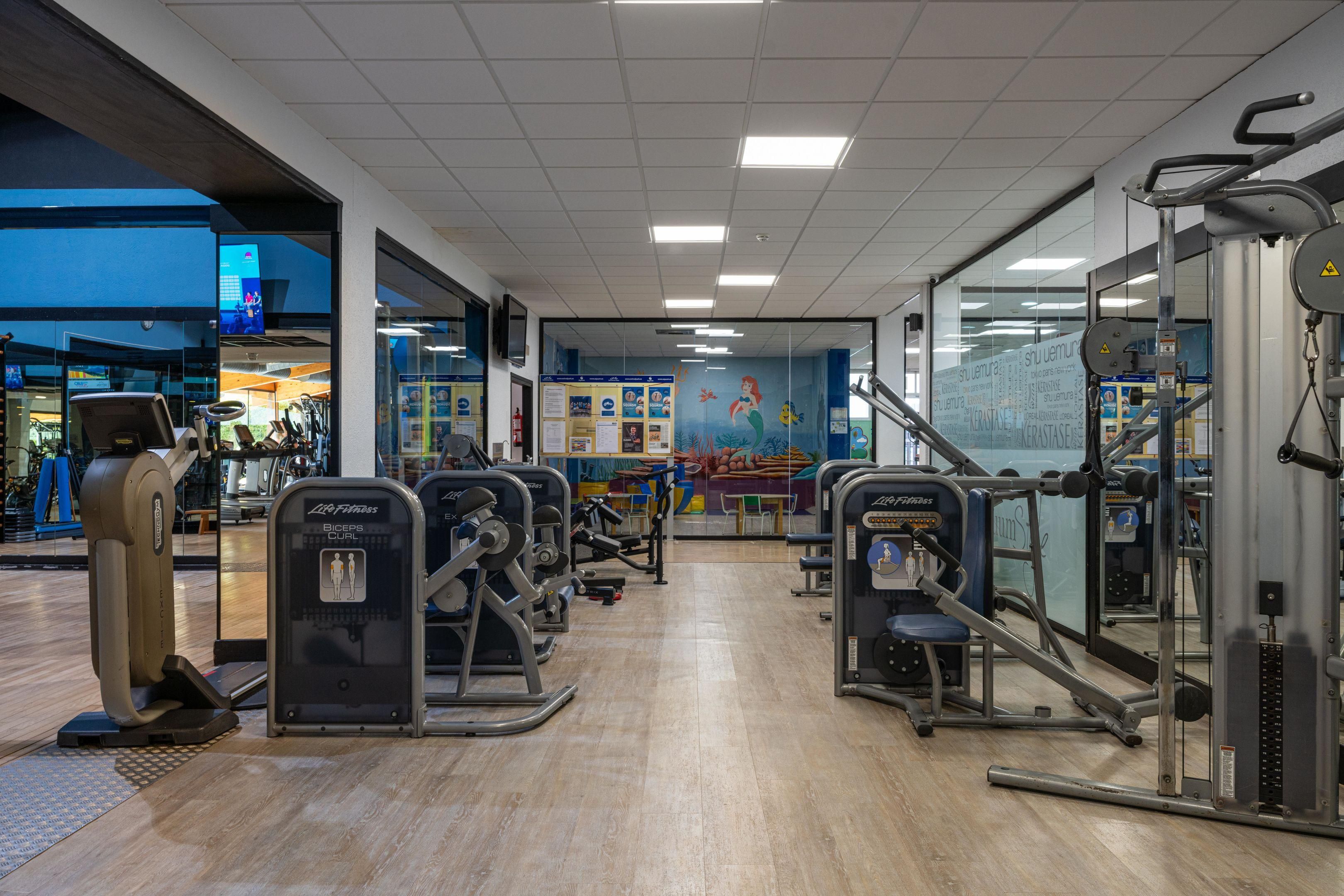 A gym with various exercise machines, a mural on the wall, and a wooden floor.