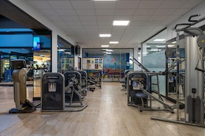 Un gimnasio con diversas máquinas de ejercicio, un mural en la pared y piso de madera.